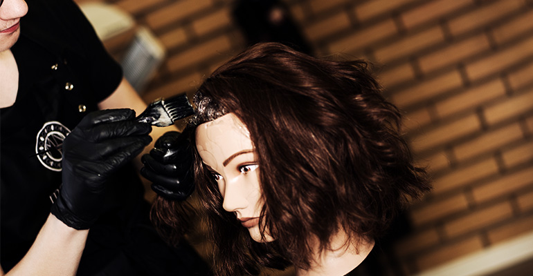 Bild på elev som färgar håret på en frisördocka.