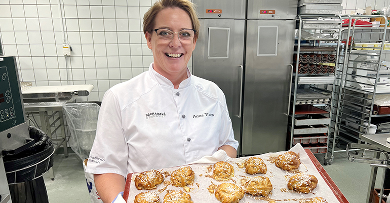 Bageriläraren Anna Thörn står i vitt bagarrock och håller en plåt med nygräddade kanelbullar.